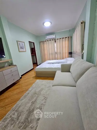 Spacious bedroom with modern decor and natural light, featuring a comfortable bed and stylish sofa.