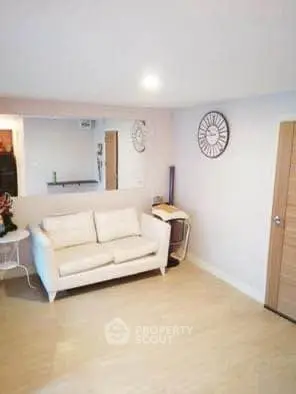 Charming living room with cozy white sofa and stylish wall clock, perfect for relaxation.