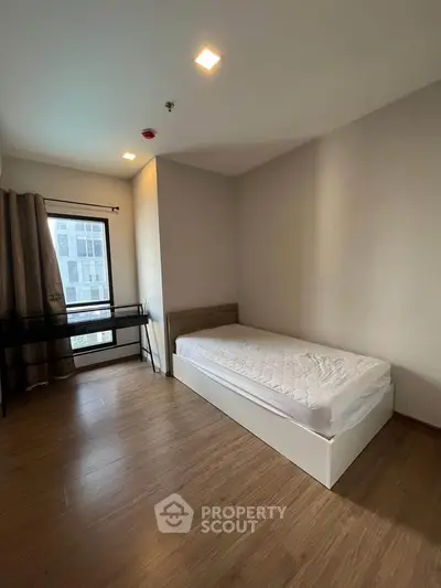 Modern minimalist bedroom with single bed and wooden flooring, featuring a large window for natural light.