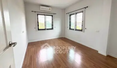 Spacious empty room with wooden flooring and large windows, perfect for customization.