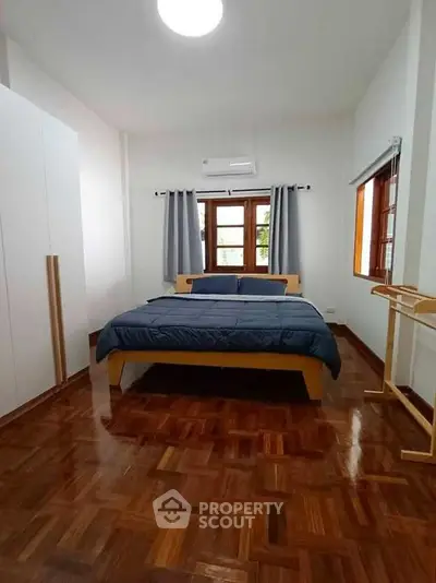 Spacious bedroom with wooden flooring and large windows for natural light.