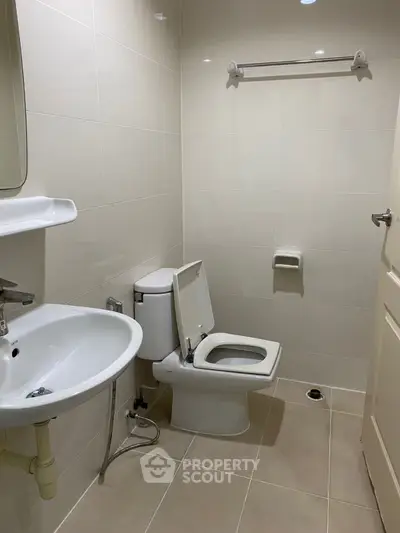 Modern bathroom with sleek fixtures and neutral tiles, featuring a toilet and sink.