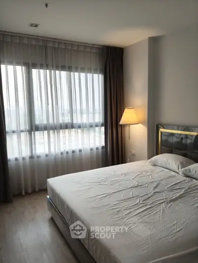 Modern bedroom with large window and stylish lamp in a high-rise apartment.