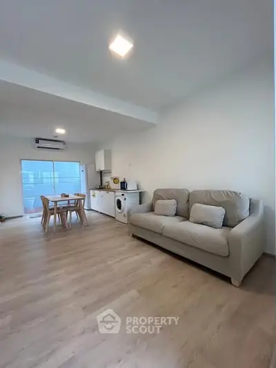 Spacious modern living room with open kitchen and dining area, featuring light wood flooring and cozy seating.