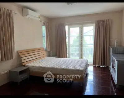 Spacious bedroom with wooden flooring and balcony access in a modern home.