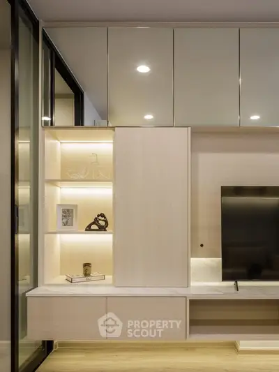 Modern living room with sleek built-in shelving and flat-screen TV, featuring elegant lighting and minimalist decor.