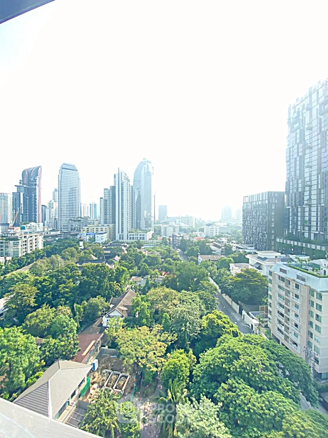 Stunning cityscape view from high-rise building with lush greenery and modern skyscrapers.