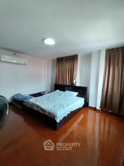 Spacious bedroom with wooden flooring and natural light, featuring a cozy bed and air conditioning.