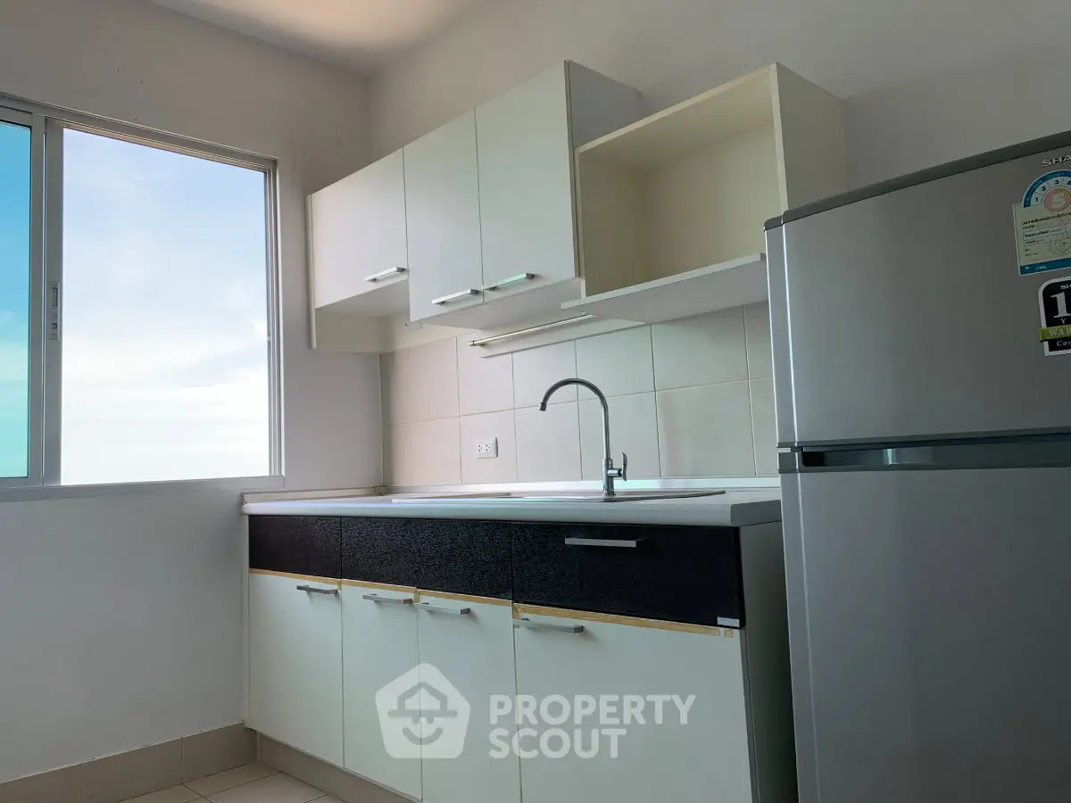 Modern kitchen with sleek cabinets and stainless steel fridge, featuring a large window for natural light.