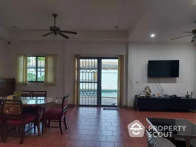 Spacious living room with red tiled flooring, large windows, and a ceiling fan, leading to a sunny balcony with a view.