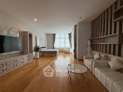 Spacious modern living room with wooden flooring, large TV, and elegant furniture.