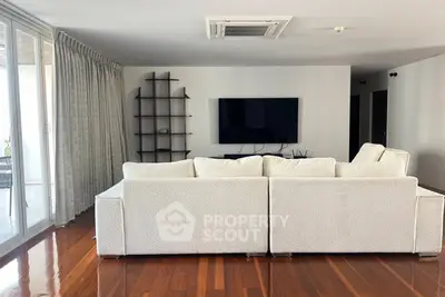 Spacious living room with modern decor and large TV, featuring elegant wooden flooring and ample natural light.