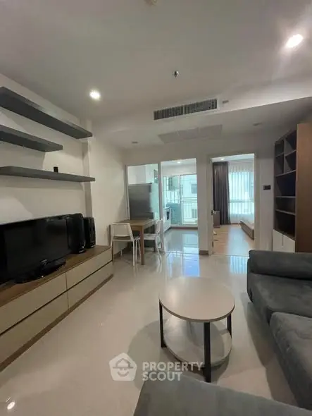 Modern living room with sleek furniture and open layout leading to kitchen and bedroom.