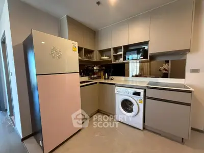 Modern kitchen with sleek cabinetry, washing machine, and large fridge in stylish apartment.
