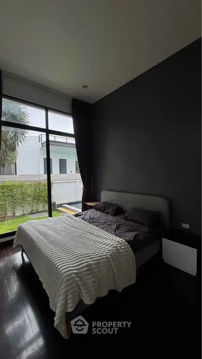 Modern bedroom with large window and garden view, featuring a cozy bed and dark accent wall.