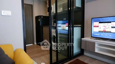 Modern living room with glass partition, washing machine, and TV setup in a cozy apartment.