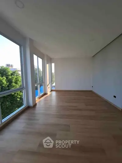 Spacious empty room with large windows and wooden flooring, offering abundant natural light and serene views.
