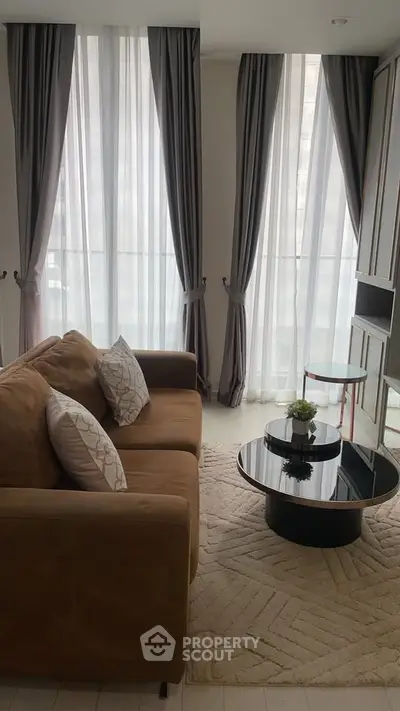Elegant living room with plush sofa, stylish coffee table, and floor-to-ceiling windows with curtains.