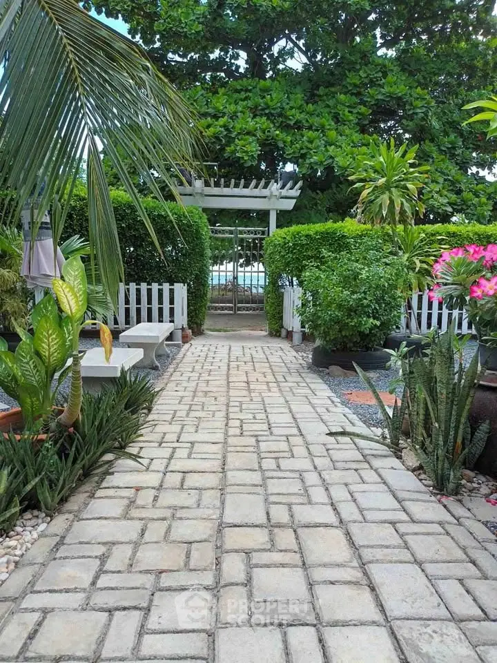 Charming garden pathway leading to a serene outdoor space with lush greenery and a glimpse of the sea.