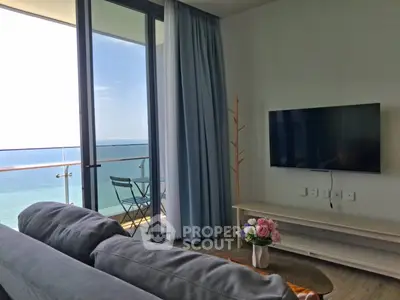 Modern living room with ocean view and balcony access, featuring sleek furniture and a wall-mounted TV.