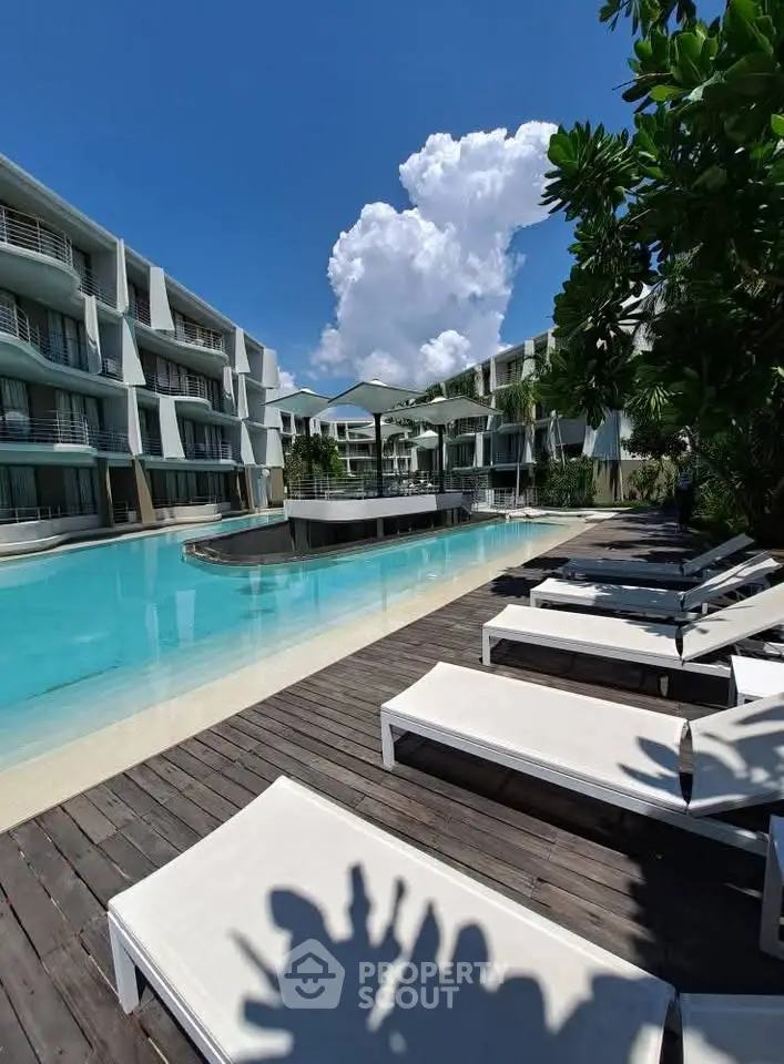 Luxurious poolside view at modern apartment complex with sun loungers and lush greenery.