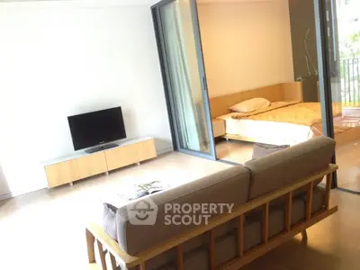 Modern open-plan living room with cozy sofa and TV, leading to a bright bedroom with balcony access.