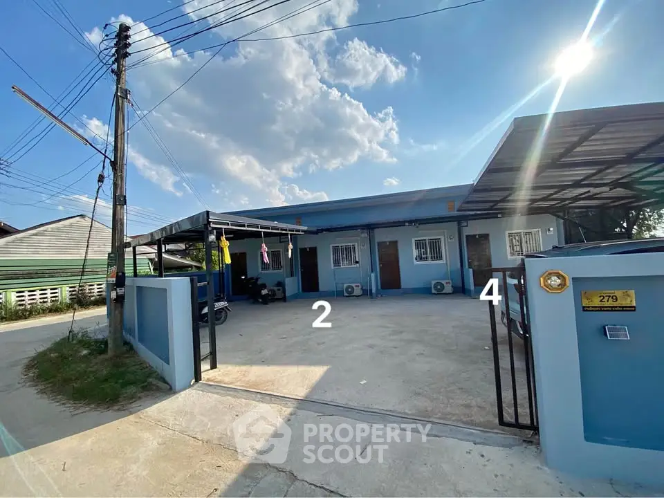 Charming single-story blue house with gated entrance and spacious driveway under a sunny sky.