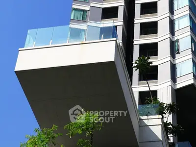 Modern high-rise building with spacious balcony and glass railings against clear blue sky.