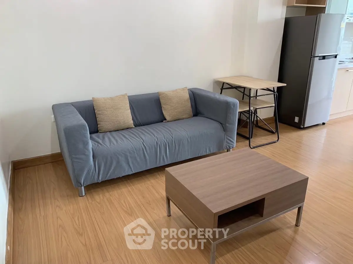 Modern living room with stylish sofa, wooden coffee table, and sleek kitchen area with fridge.
