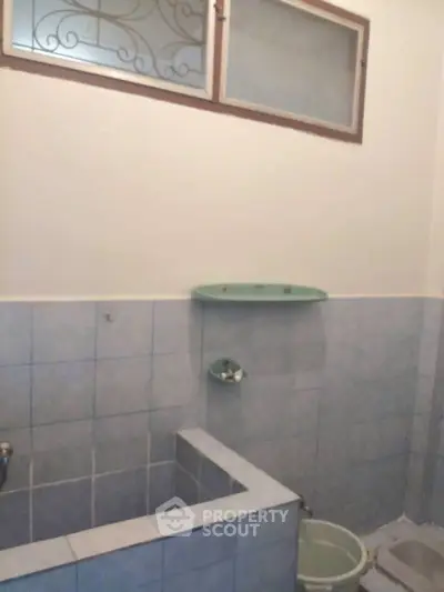 Simple bathroom with tiled walls and small glass shelf.
