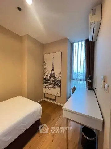Cozy bedroom with wooden flooring, desk, and large window offering natural light.