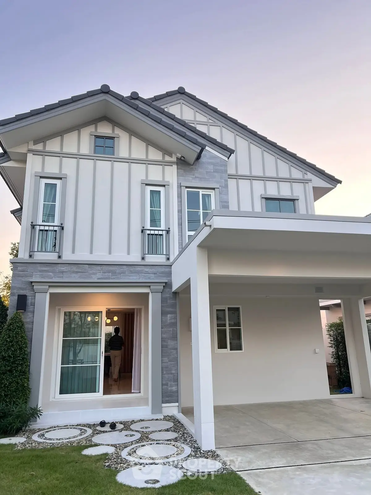 Modern two-story house with elegant facade and spacious driveway at sunset.