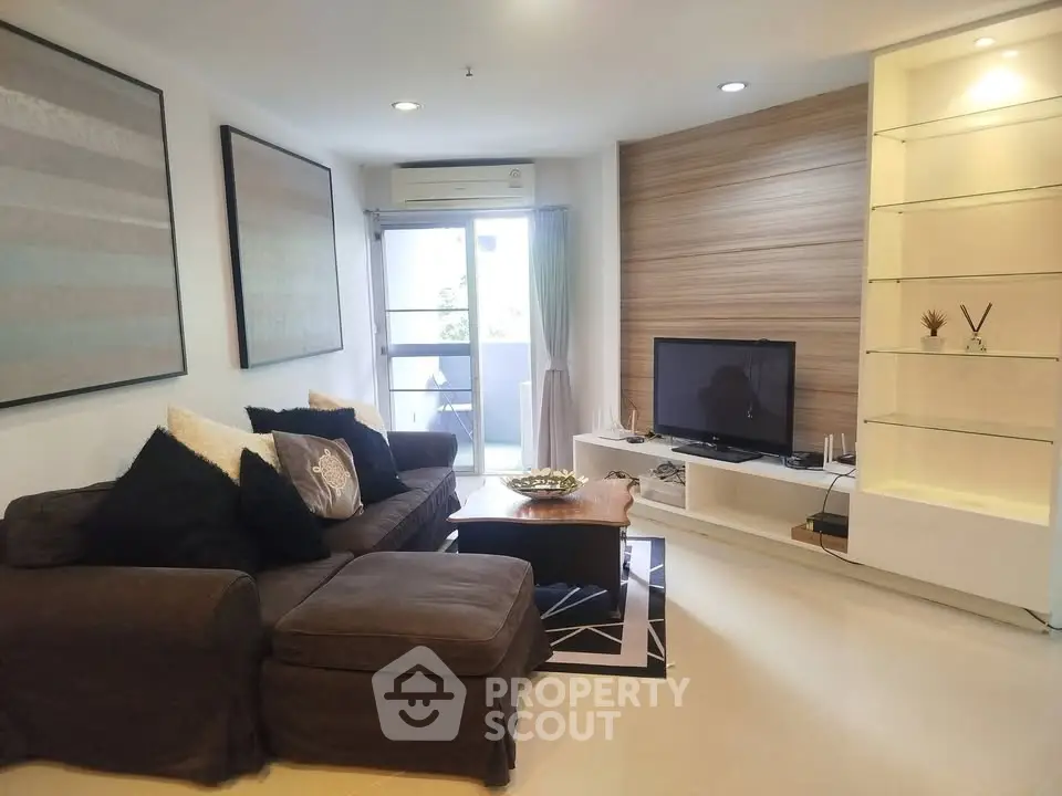 Modern living room with cozy sofa and TV, featuring stylish decor and natural light from balcony.