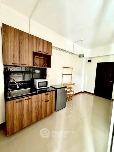 Compact kitchen with wooden cabinets, microwave, and mini fridge in a bright apartment.
