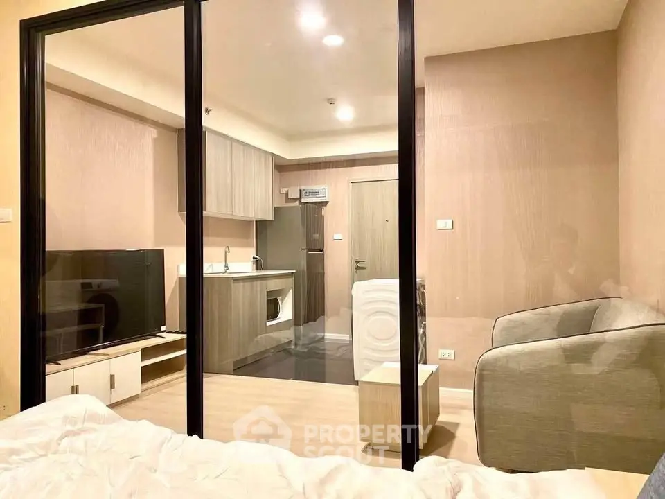 Modern studio apartment with glass partition, cozy living area, and compact kitchen.