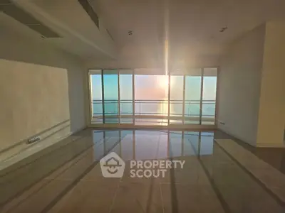 Spacious sunlit living room with floor-to-ceiling windows and stunning ocean view.