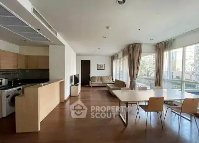 Spacious modern living room with open kitchen and dining area, featuring large windows and natural light.