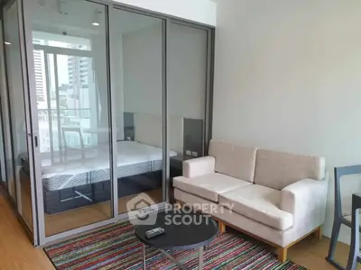Modern apartment with glass-walled bedroom and cozy living area, featuring a stylish sofa and vibrant rug.