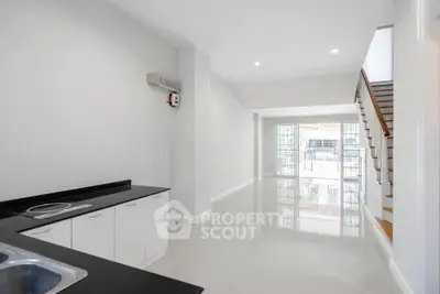 Spacious modern living room with sleek kitchen and staircase, featuring large windows for natural light.