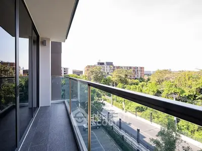 Modern balcony with glass railing offering a scenic view of lush greenery and urban landscape.