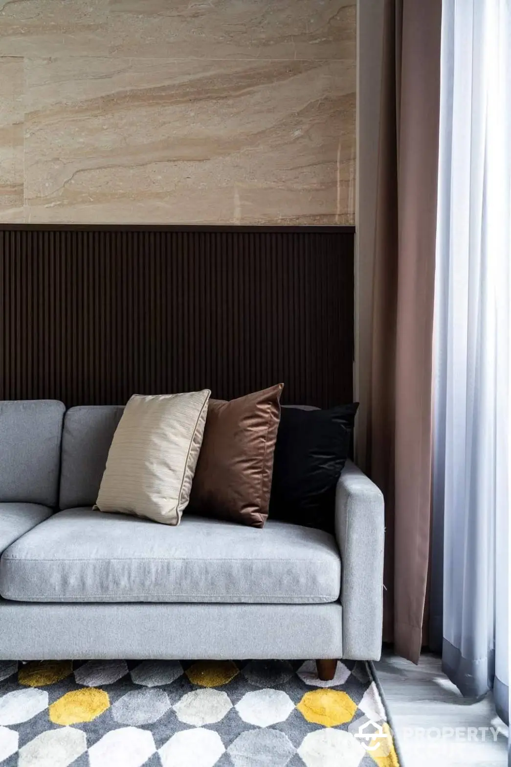 Elegant living room corner with a plush grey sofa, stylish patterned rug, and a harmonious blend of natural stone wall and wooden paneling.