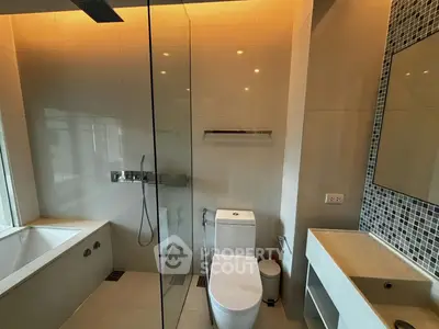 Modern bathroom with glass shower, bathtub, and sleek fixtures in a contemporary apartment.