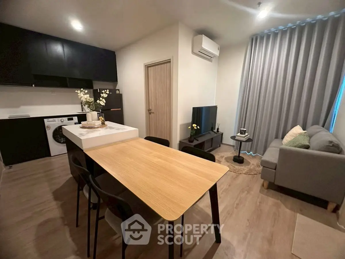 Modern open-plan living room with kitchen, featuring sleek furniture and appliances.