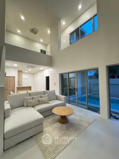 Luxurious modern living room with high ceilings and pool view, featuring elegant furniture and large windows.