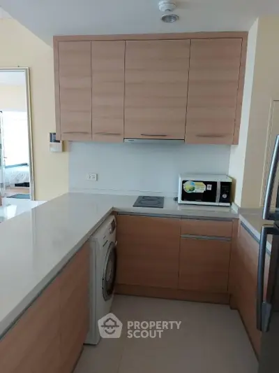 Modern kitchen with wooden cabinets, washing machine, and microwave in a compact layout.