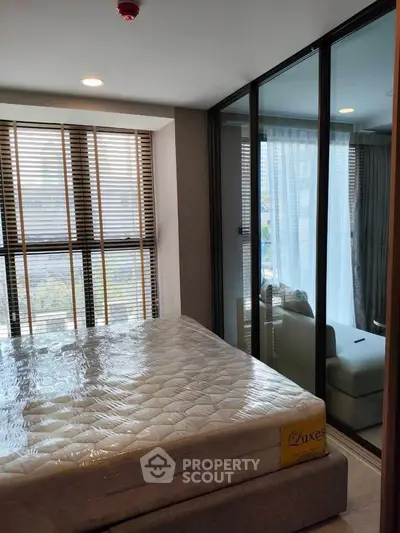 Modern bedroom with large windows and glass partition, featuring a new mattress and cozy seating area.