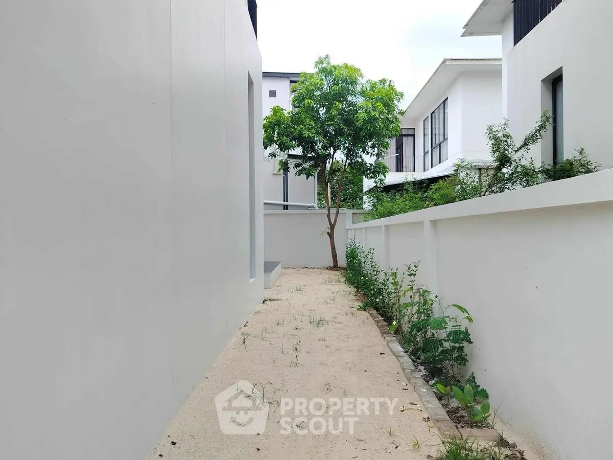 Modern minimalist exterior with white walls and greenery in a residential area.