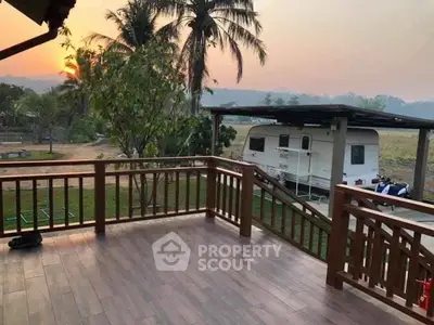 Charming wooden balcony with scenic countryside view and caravan in the background.