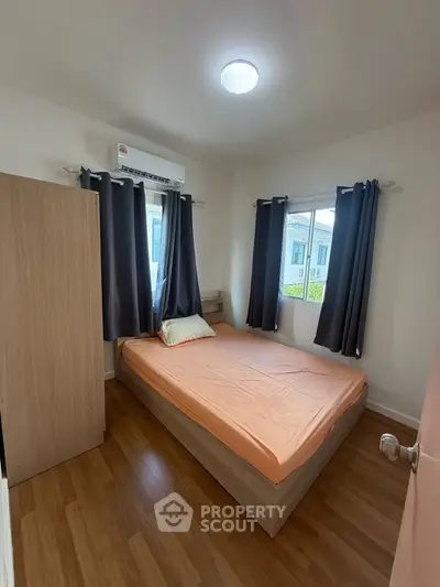 Cozy bedroom with wooden flooring and natural light from two windows.