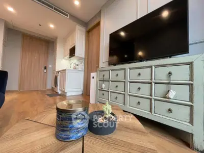 Modern living room with stylish decor and wooden flooring, featuring a TV and compact kitchen area.